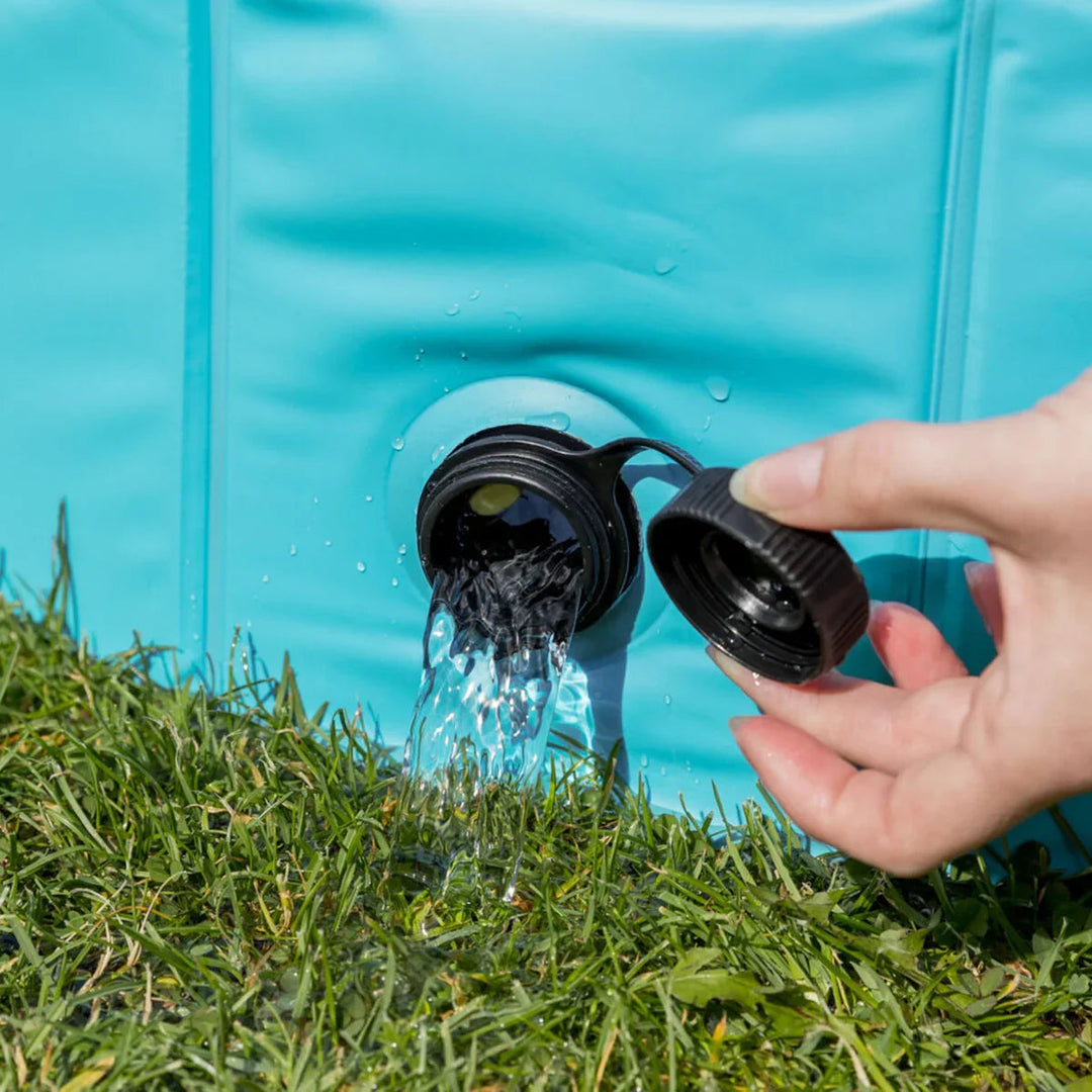 Hand opening black spout on turquoise water container pouring water onto green grass zigly