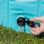 Hand opening black spout on turquoise water container pouring water onto green grass zigly