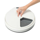 Hand adjusting white and gray round smart pet feeder with zigly design