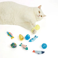 White cat lying on white background with colorful fish and ball toys, holding yellow toy, zigly